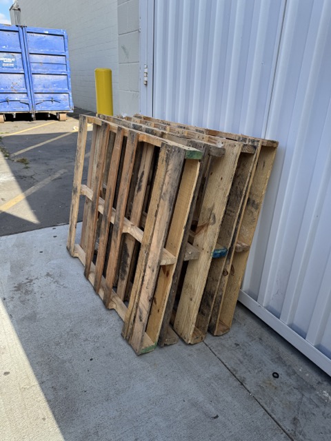 Wooden pallets stacked against a warehouse wall for bulk pallet removal