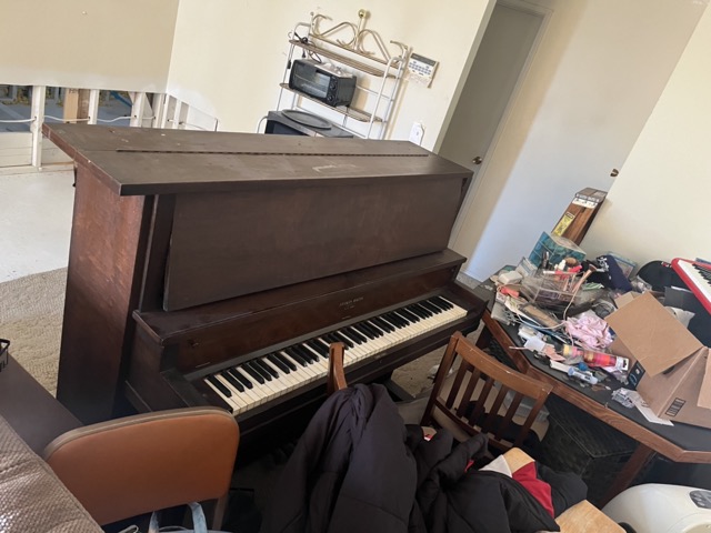 Upright piano in a cluttered room ready for junk removal